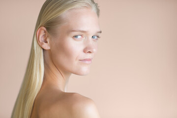Topless blonde female model staring with beautiful eyes into the camera. Isolated against a rose gold background. Beauty, hair and skin care cosmetics.