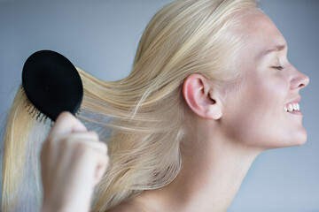 Hair care beauty. Happy content female model brushing her silky smooth blonde hair. Isolated side-view profile.