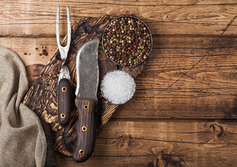 Vintage fork and knife for meat on wooden chopping board with salt and pepper on wooden table background with linen towel.