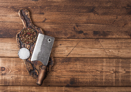 Vintage hatchet for meat on wooden chopping board with salt and pepper on wooden table background. Space for text