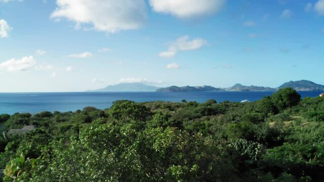 Drone camera captures the tops of dense forest and view of blue sea and mountains in Saint Kitts and Nevis