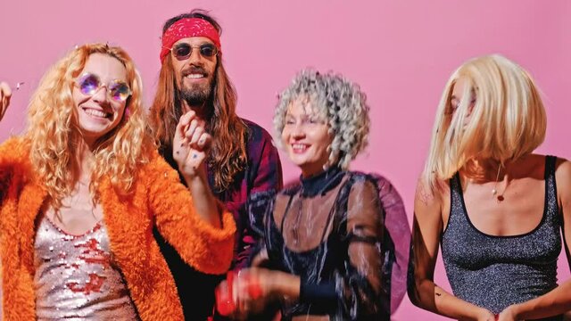 Three girls and one guy had a party and threw confetti and had fun on a background of a pink wall. People are dressed in clothes of different subcultures from the 60's, 70's, 80's and 90's.