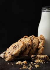 Homemade organic oatmeal cookies with raisins and apricots and bottle of milk on dark wooden background.