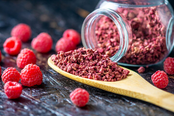 Freeze dried raspberries in a glass jar and a wooden spoon on a black background. Concept of berry...