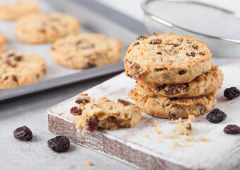 Homemade organic oatmeal cookies with raisins and apricots with baking tray on light background.