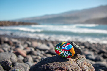 Painted stone in different colors with the inscription: Be happy. Ocean view.