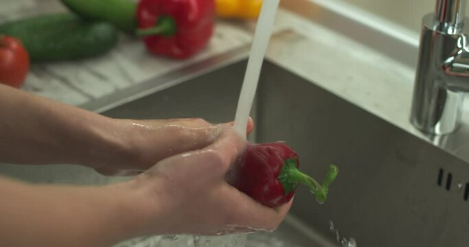 Female hands wash red Ramiro pepper by stream of water. Close up