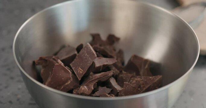 Slow motion handheld shot of young woman put cocolate crumbs in steel bowl closeup