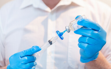 Shallow depth of field close up image of medical doctor wearing blue medical gloves holding a syringe, filter and vial 