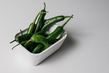 Hot green peppers in a white bowl on a white kitchen counter