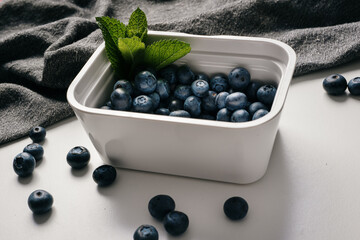Blueberries in a white container with mint on white kitchen countertop with gray kitchen towel