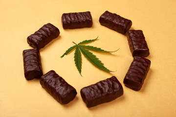 chocolate candy with green leaf marijuana plant on a yellow background. sweets and cannabis