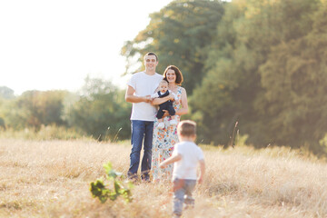 Family with children walking outdoors in summer field at sunset. Father, mother and two children sons having fun in summer field. People, family day and lifestyle concept