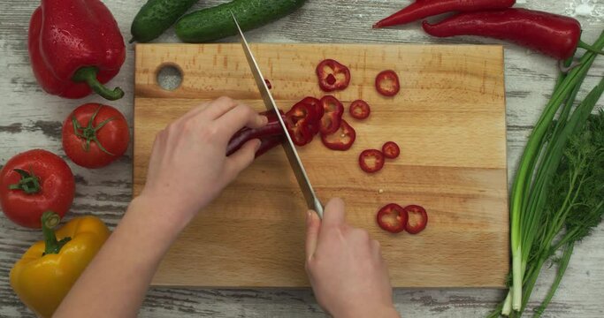 Female hands cut fresh red Ramiro pepper into round pieces. Top view.
