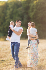 Family with children walking outdoors in summer field at sunset. Father, mother and two children sons having fun in summer field. People, family day and lifestyle concept