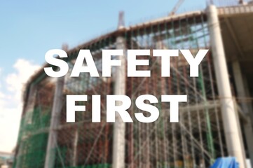 The word SAFETY FIRST is written clearly and against the background of the image of a worker installing a scaffolding. The image has been blurred.
