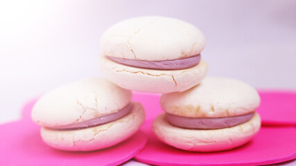 White macaroons with purple berry filling on pink background