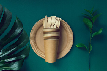 Eco friendly craft paper tableware on green background with monstera leaf. Recycling concept.