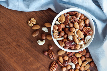 Wooden bowl with mixed nuts on table top view. Healthy food and snack. Walnut, pistachios, almonds, hazelnuts and cashews.