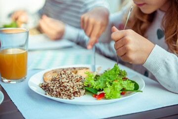 Fototapeta na wymiar Close up photo of hands of child girl eating healthy dinner with salad, quinoa and fish