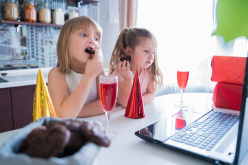 Kids virtual birthday party.Girls in dresses and caps celebrate holiday with friends on isolation.Online conference,video call in laptop,computer.Animator,juice,cookies.Quarantine,coronavirus covid-19