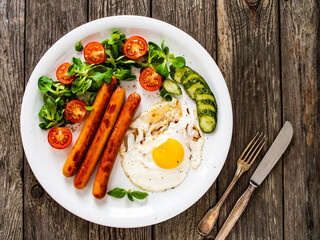 Breakfast - sunny side up egg, fried sausages and vegetables served on wooden table
