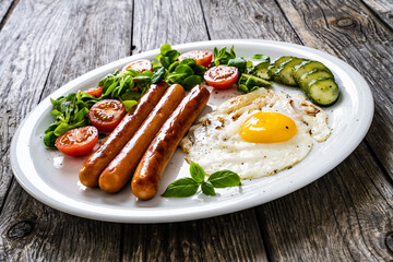 Breakfast - sunny side up egg, fried sausages and vegetables served on wooden table
