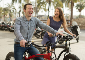 Fototapeta na wymiar couple guy with a girl ride bicycles with thick wheels in the summer along the promenade