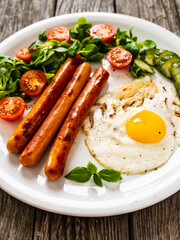 Breakfast - sunny side up egg, fried sausages and vegetables served on wooden table

