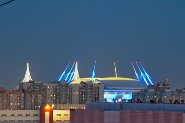 Night view of the Zenith Arena stadium in St. Petersburg during the white nights. The towers look colorful in the background of the light blue sky.