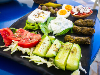 Crete plate - fresh Greek salad, feta cheese, dolmades, tomatoes, lettuce, boiled egg, black and green olives on black plate