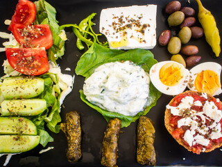 Crete plate - fresh Greek salad, feta cheese, dolmades, tomatoes, lettuce, boiled egg, black and green olives on black plate