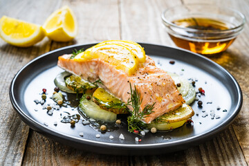 Roasted salmon steak with lemon and onion served on black plate on wooden table
