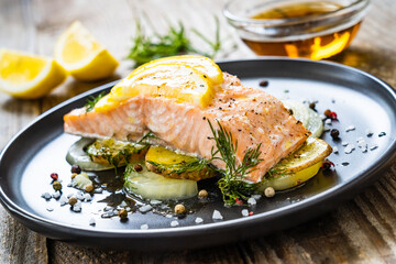 Roasted salmon steak with lemon and onion served on black plate on wooden table

