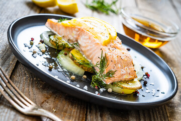 Roasted salmon steak with lemon and onion served on black plate on wooden table
