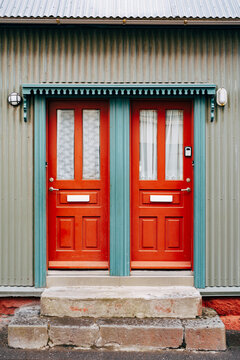 Two orange entrance doors with glass and curtains in a blue doorway.