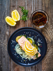 Roasted salmon steak with lemon and onion served on black plate on wooden table
