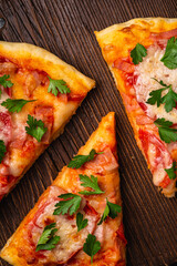 Hot pizza slices with mozzarella cheese, ham, tomato and parsley on brown wooden cutting board, top view macro