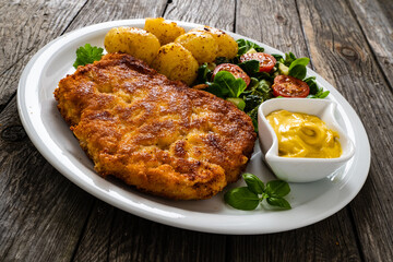 Breaded pork chop with boiled potatoes and vegetable salad on wooden background
