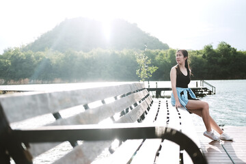 Beautiful young sexy asian woman relaxing and sitting on wooden bridge lonely in the park with natural sunlight and lake on Summertime. Lifestyle and vacation on holiday Concept.