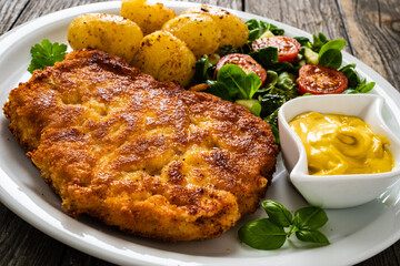 Breaded pork chop with boiled potatoes and vegetable salad on wooden background
