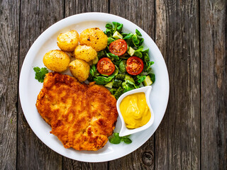 Breaded pork chop with boiled potatoes and vegetable salad on wooden background
