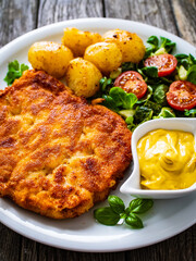 Breaded pork chop with boiled potatoes and vegetable salad on wooden background
