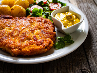Breaded pork chop with boiled potatoes and vegetable salad on wooden background

