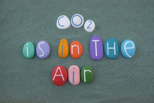 Naklejki CO2 is in the air, slogan text composed with multicolored stone letters over green sand