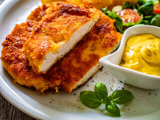 Breaded pork chop with boiled potatoes and vegetable salad on wooden background
