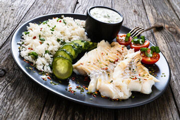 Fish dish - fried cod fillet with basmati rice and vegetables on wooden table
