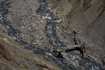 A wooden trail bridge over Marsyangdi river broken by flood and landslide. Rocks, debris and gravel on the mountain river  in the high Himalayas of Nepal. 