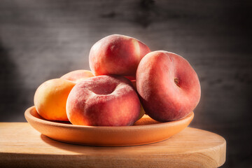 Group of delicious sweet flat donut peaches in a clay plate on old wooden table in early morning sunlight. Close up view