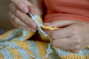 Needlework. Women's hands close up crocheting children's plaid. Crochet hook